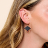 Woman wearing a black geometric leather earring with gold chain details.