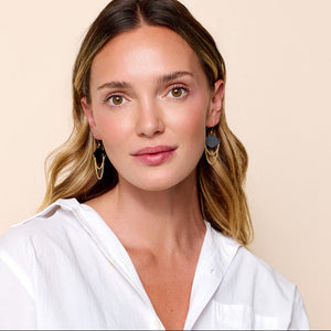 Woman wearing earrings that are black leather with looped gold chain. 